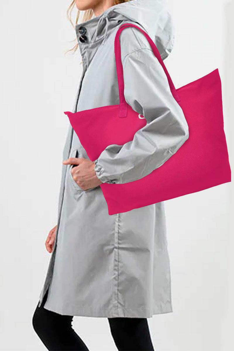 Woman in gray raincoat carrying large pink waterproof travel bag over shoulder