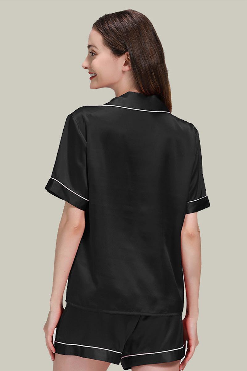 Woman wearing black Mulberry Silk Essentials buttoned short set nightwear with white piping trim, shown from the back.