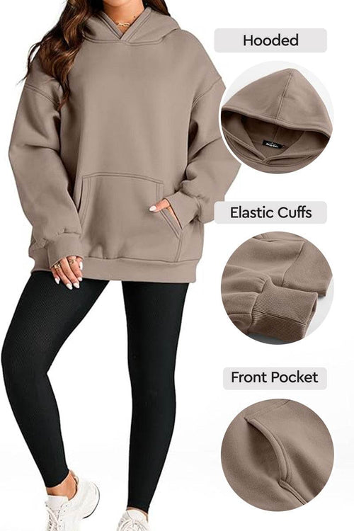 Woman wearing oversized fleece-lined hoodie with hood, elastic cuffs, and front pocket in taupe color paired with black leggings and white sneakers