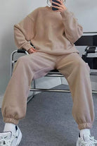 Woman wearing beige comfy chic tracksuit with relaxed fit and elastic cuffs sitting on chair