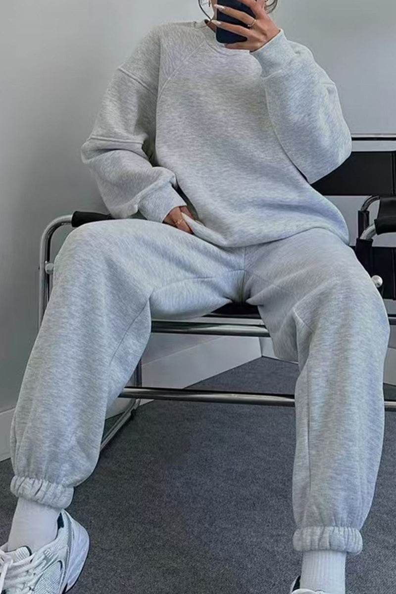 Woman wearing light gray comfy chic tracksuit with relaxed fit, sitting on chair, styled with white sneakers.