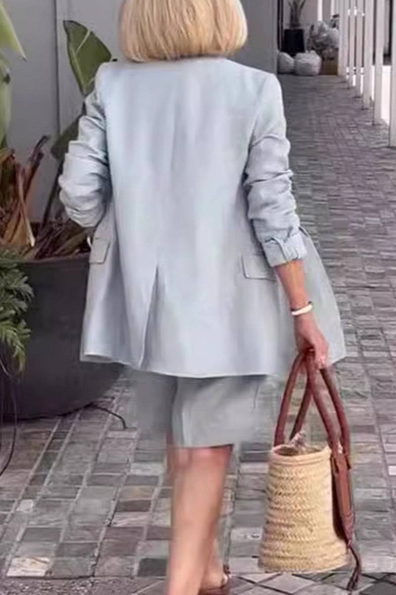 Woman wearing stylish blazer and shorts two-piece set walking on tiled path carrying woven bag