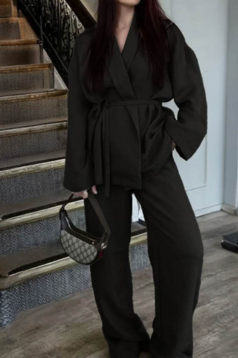 woman wearing black versatile mix-match lounge-to-travel set with wide-leg pants and belted top holding handbag indoors near stairs