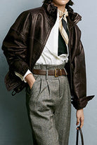 Woman wearing a dark brown genuine sheepskin leather jacket with ruffled collar and gray high-waisted pants.