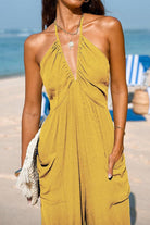 Woman wearing Sunshine On Sand yellow ruched halter-neck jumpsuit at the beach with pockets and adjustable ankle cuffs