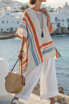 Woman wearing Coastal Comfort Linen two-piece set with a loose, colorful striped top and white wide-leg pants by the seaside with a round woven bag.