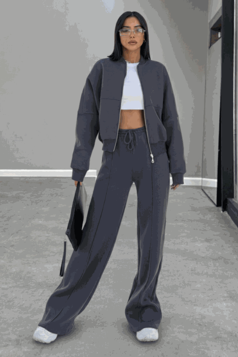 Woman wearing The Voyager Zip Set in charcoal gray, featuring a relaxed zip-front sweatshirt and wide-leg joggers with pockets, styled with white sneakers and a tote bag.