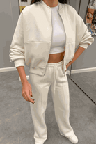 Woman wearing The Voyager Zip Set cream zip-front sweatshirt and wide-leg joggers with pockets, styled with a white crop top and sneakers.