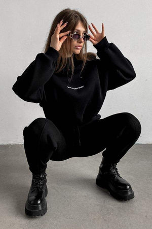 Woman wearing black Storm Sweater Mock Neck athleisure set with relaxed fit and boots against gray background