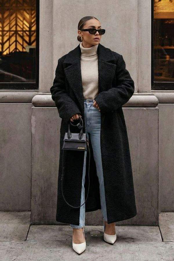 Woman wearing a black oversized teddy coat with longline silhouette, paired with jeans and white heels.