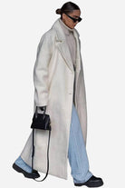 Woman wearing an oversized white teddy coat with turtleneck, light blue jeans, sunglasses, and black handbag.