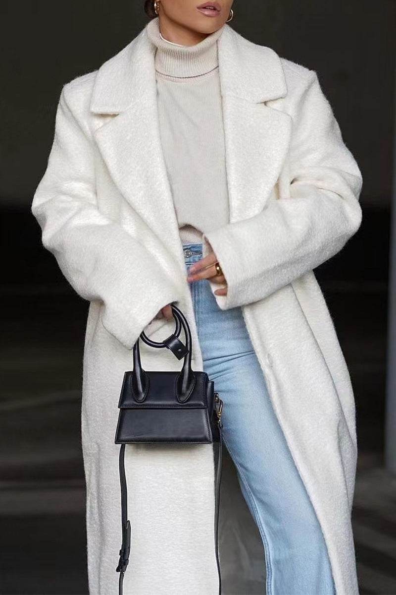 Woman wearing white oversized teddy coat with wide lapels, paired with light turtleneck and jeans, holding small black handbag