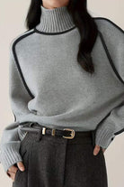 Woman wearing gray Zero Itch Turtleneck Sweater with black contrast trim and dark trousers