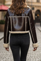 Back view of a cropped faux leather sherpa jacket with cream sherpa trim on cuffs and hem, worn with black jeans on a city street.