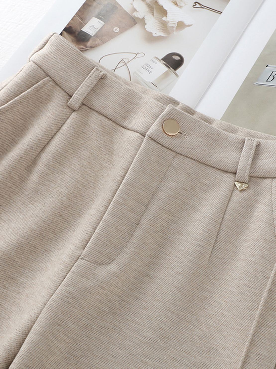 Close-up of beige thermal wool blend trousers with button and belt loops on a flat surface
