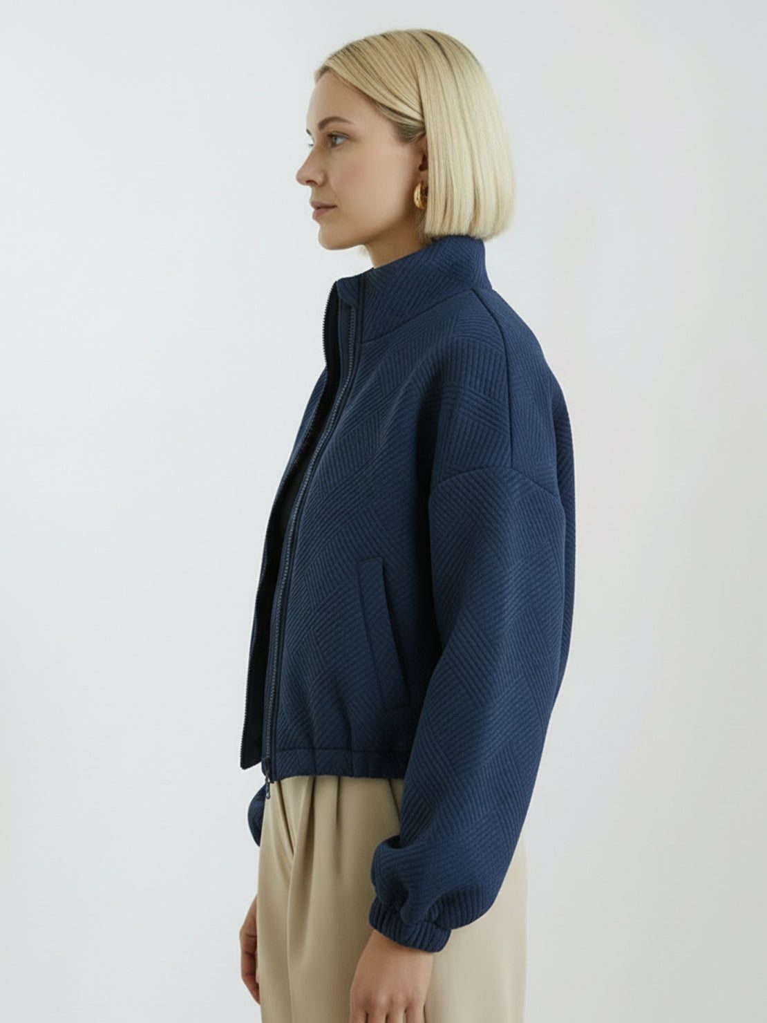 Cropped textured baseball jacket with full zipper and elastic cuffs, styled with high-waisted pants.