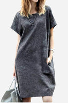Woman wearing a charcoal gray short sleeve shift dress with side pockets, accessorized with a necklace and gray handbag