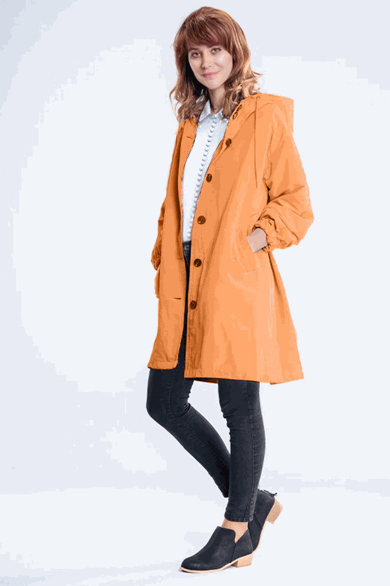Woman wearing orange water resistant oversized windbreaker jacket with hood and black buttons