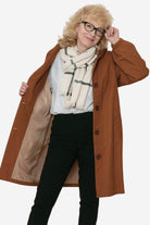 Woman wearing brown water resistant oversized windbreaker open with scarf and glasses against white background