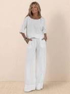 Woman wearing white short-sleeved pullover and wide trouser matching set made of lightweight cotton with deep pockets and cuffed hems.