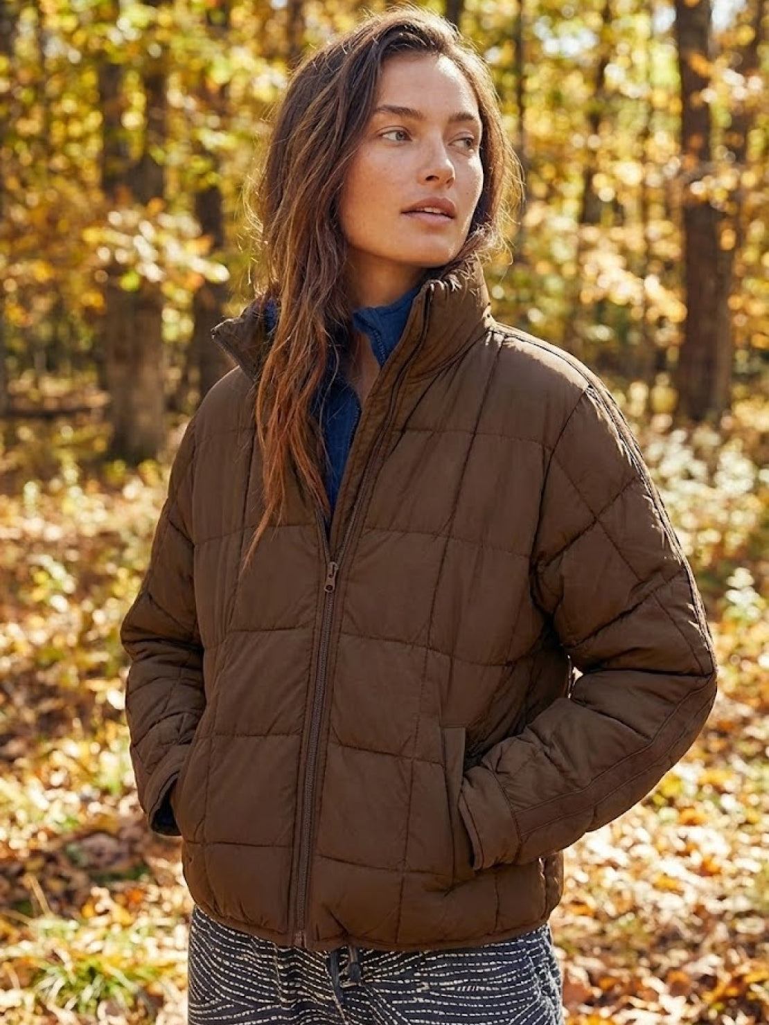 Woman wearing lightweight brown puffer travel jacket in autumn forest setting
