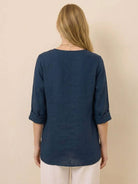 Back view of a woman wearing a navy blue Pure Linen Age-Defying Shirt with rolled-up sleeves and white pants, showcasing breathable and comfortable fabric.