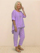 Woman wearing a lavender asymmetrical two-piece trouser set with rolled-up sleeves and tapered pants