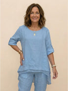 Woman wearing a light blue asymmetrical two-piece trouser set with rolled sleeves and lightweight breathable fabric.