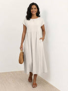 Woman wearing capped-sleeve voluminous pleated midi dress with pockets and flowing skirt