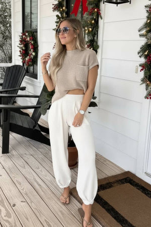 Woman wearing beige Comfy Couture Knit Sweater top and white high-waisted knit pants two-piece set on porch decorated for Christmas