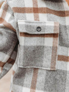 Close-up of a comfy flannel classic shirt pocket in gray, white, and brown plaid pattern with button detail