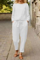 Woman wearing white cotton-linen monochrome relaxed longline top and wide-leg pants with brown sandals outdoors