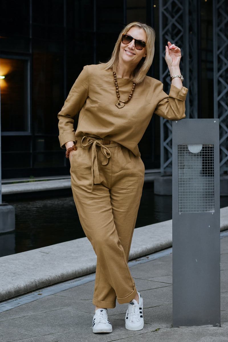 Woman wearing cotton-linen monochrome capsule outfit with longline top and wide-leg pants in tan color, accessorized with sunglasses and necklace outdoors