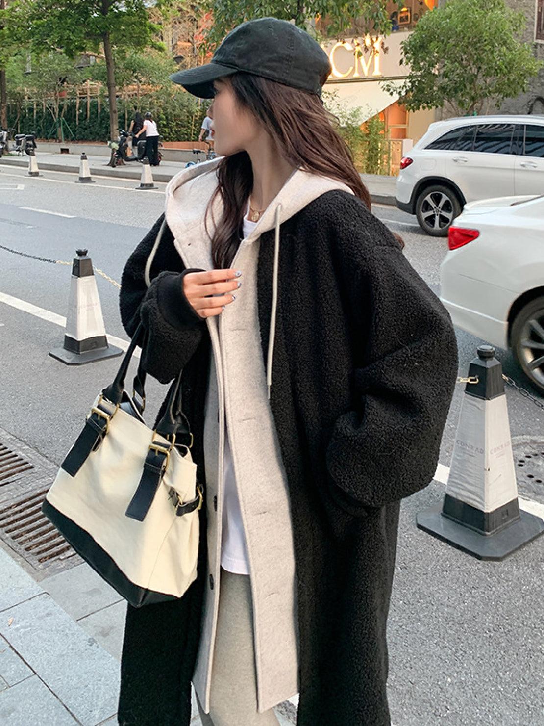 Woman wearing black everyday wear oversized sherpa coat with hoodie and carrying beige and black handbag on city street