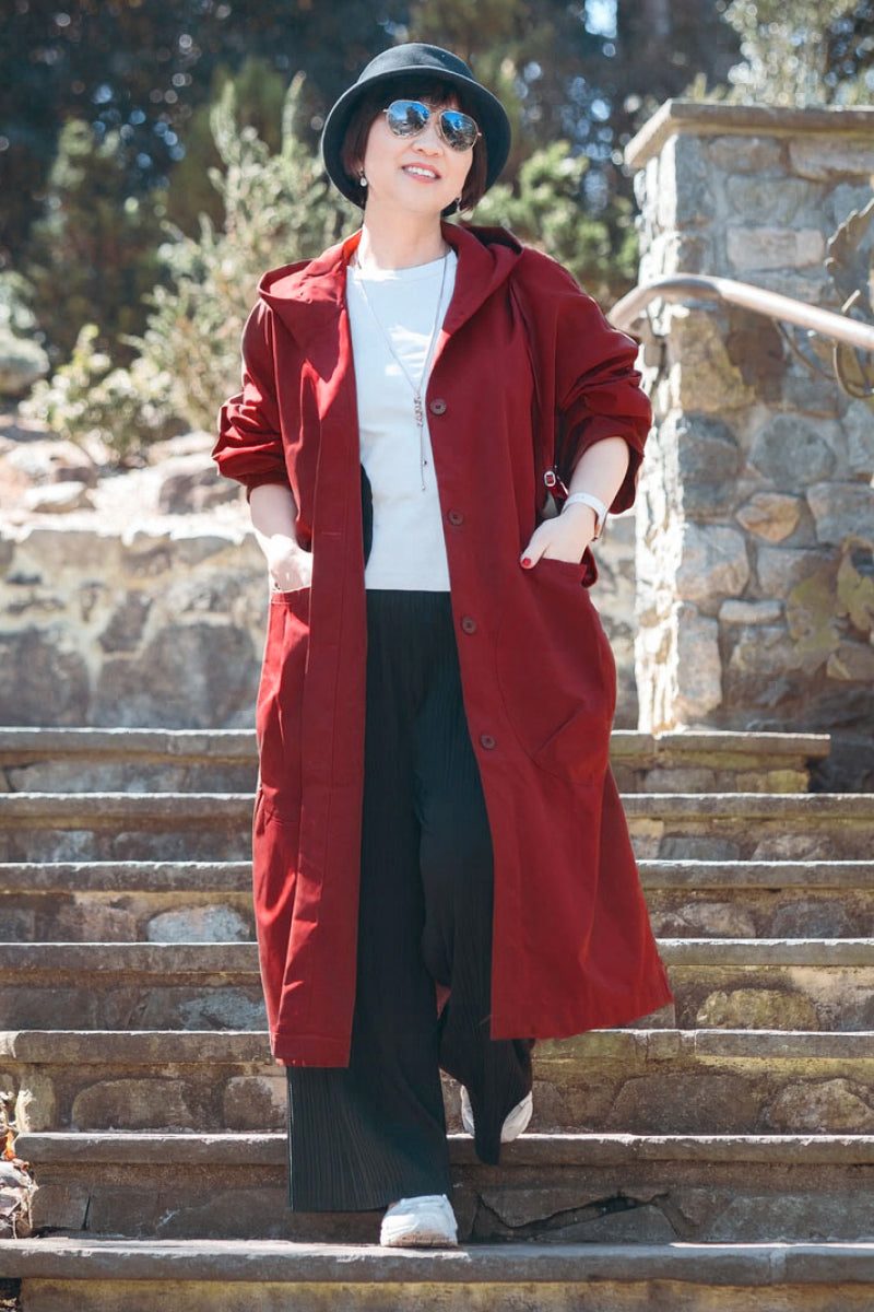 Woman wearing oversized red water resistant windbreaker jacket with hood and snap-button closure outdoors