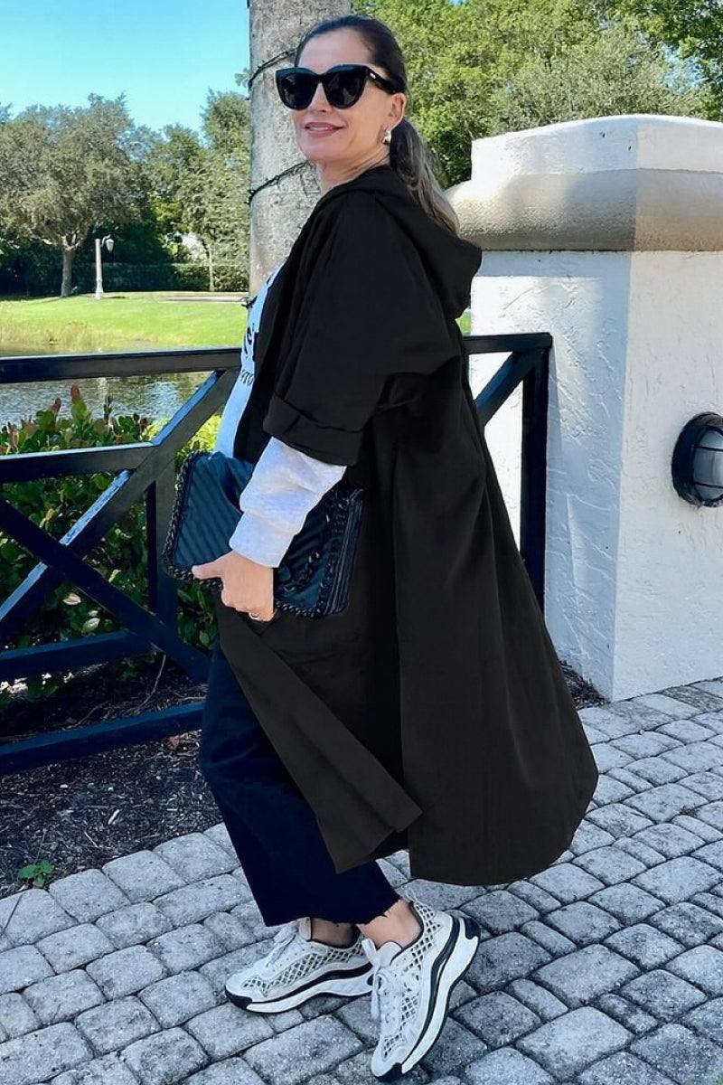 Woman wearing oversized black Heritage Windbreaker Jacket with hood, large pockets, and casual sneakers outdoors