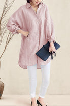 Woman wearing a pink oversized linen shirt with white pants holding a black clutch bag