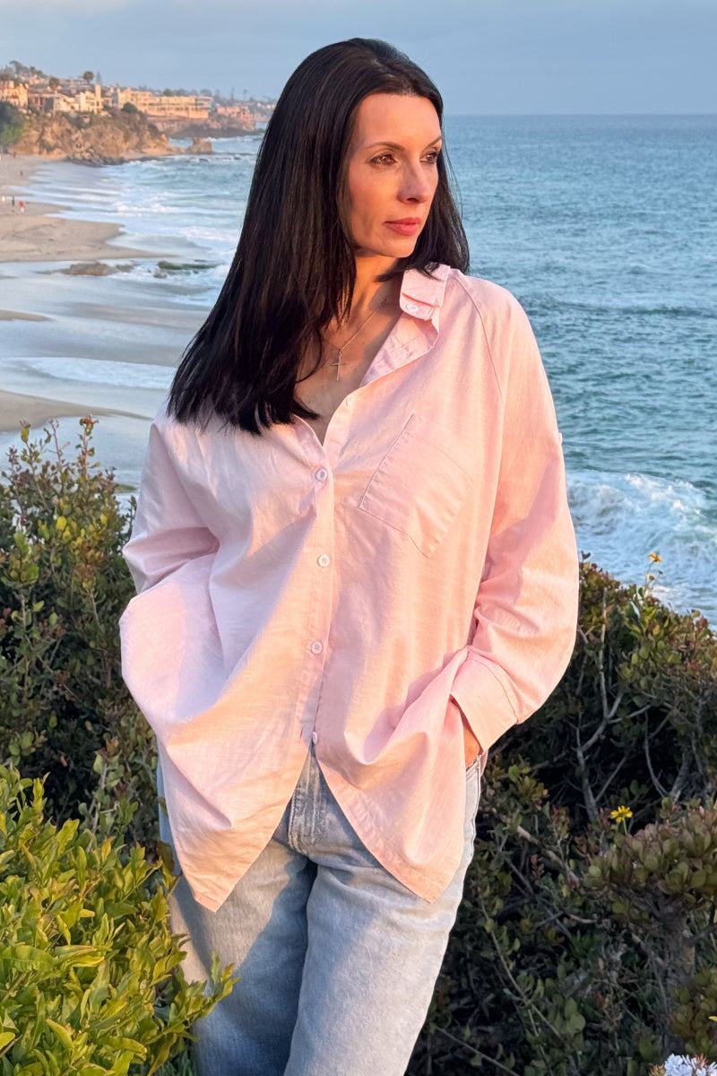 Woman wearing oversized linen shirt in sun-washed pink by the beach at sunset
