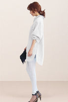 Woman wearing white oversized linen shirt with loose sleeves and flowing hemline, styled with white pants and heels.