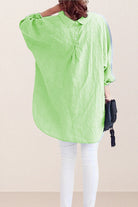 Back view of oversized linen shirt in light green with loose sleeves and buttoned back detail worn with white pants and black handbag