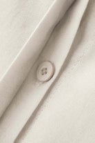 Close-up of beige oversized 100% cotton shirt fabric with button detail