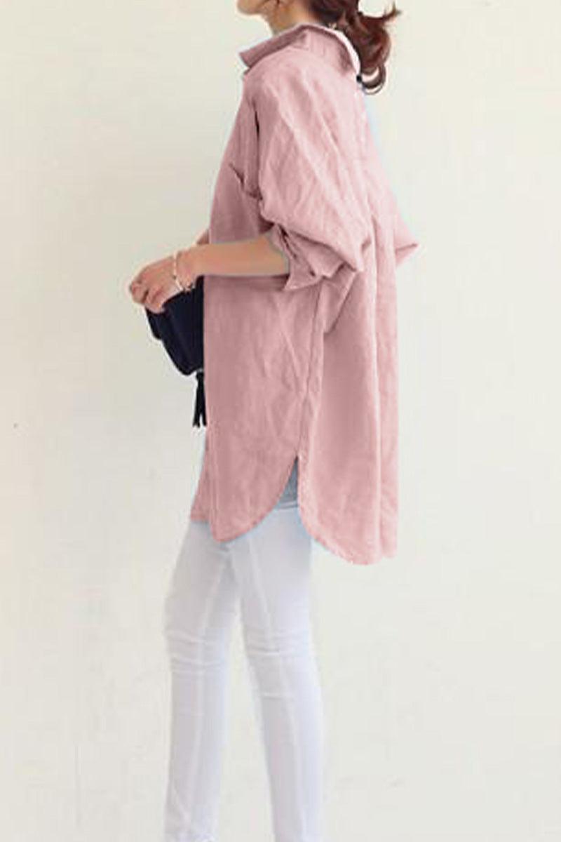 Woman wearing a pink oversized linen shirt with rolled-up sleeves and white pants, holding a black bag.