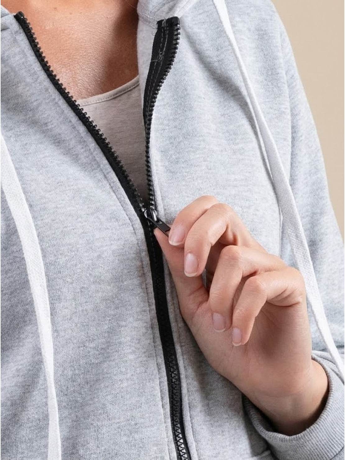 Close-up of person zipping up gray oversized long zip sweatshirt hoodie with black zipper and white drawstrings
