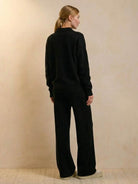 woman wearing black plush and preppy two-piece set with wide-leg pants and long sleeve top standing against beige background