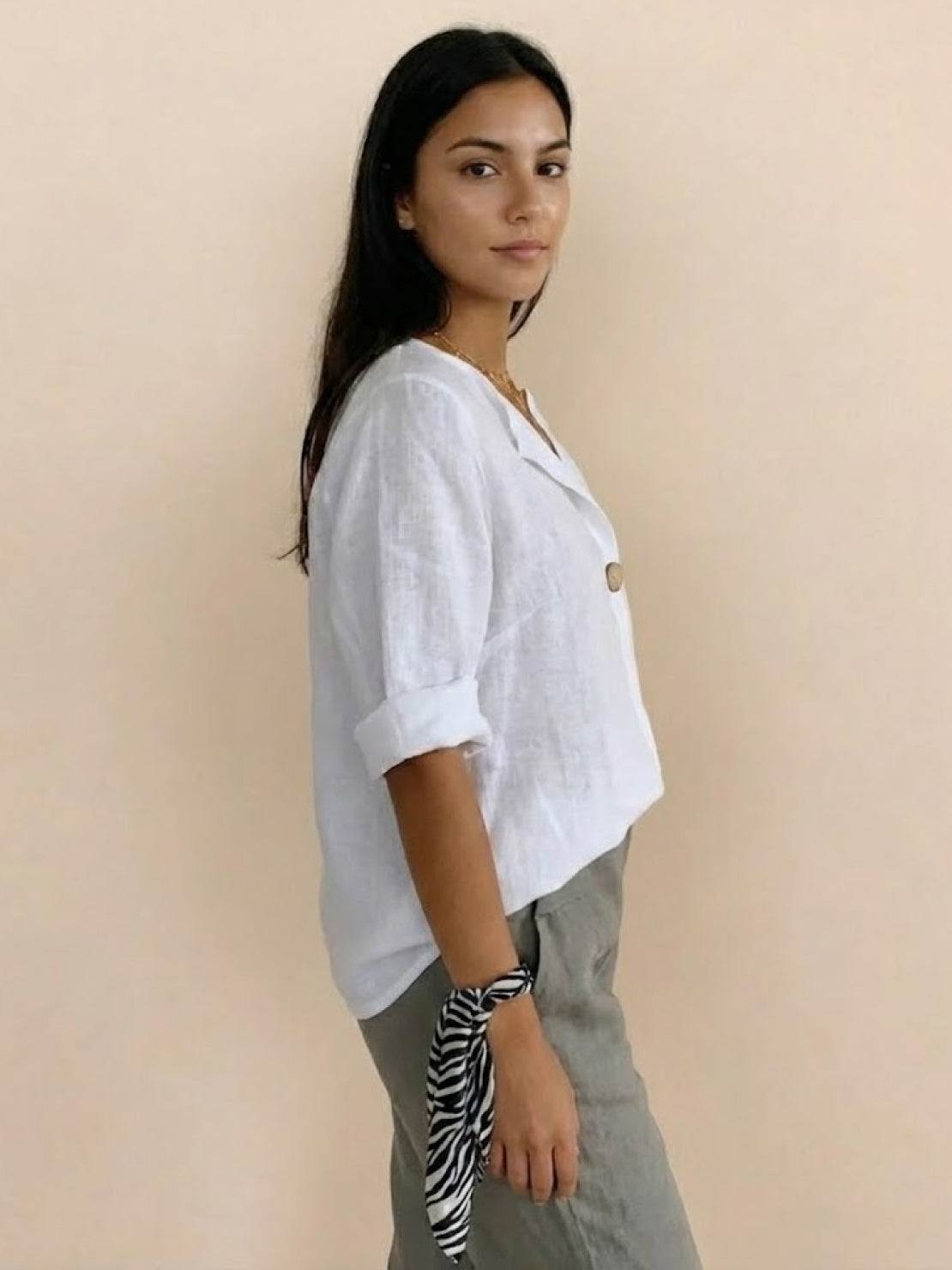 Woman wearing white pure linen age-defying shirt with button detail and rolled sleeves, paired with gray pants.