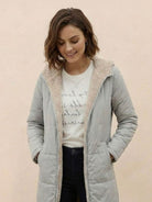 Woman wearing a light gray Sherpa-lined hooded teddy coat with soft inner lining and front pockets