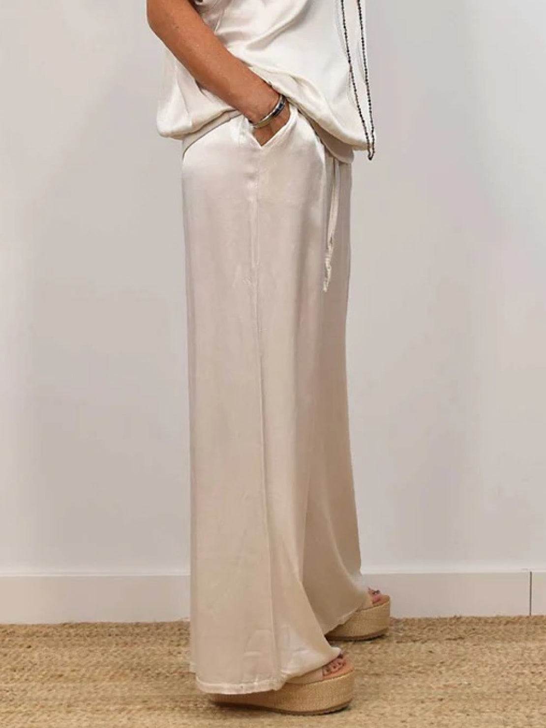 Woman wearing Silken Escape Satin Two-Piece Set with flowing satin top and wide-leg pants in elegant cream color