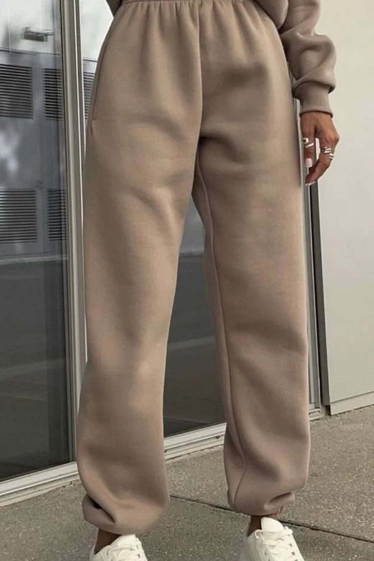 Beige cotton blend tracksuit pants with elastic waistband and cuffs styled with white sneakers.