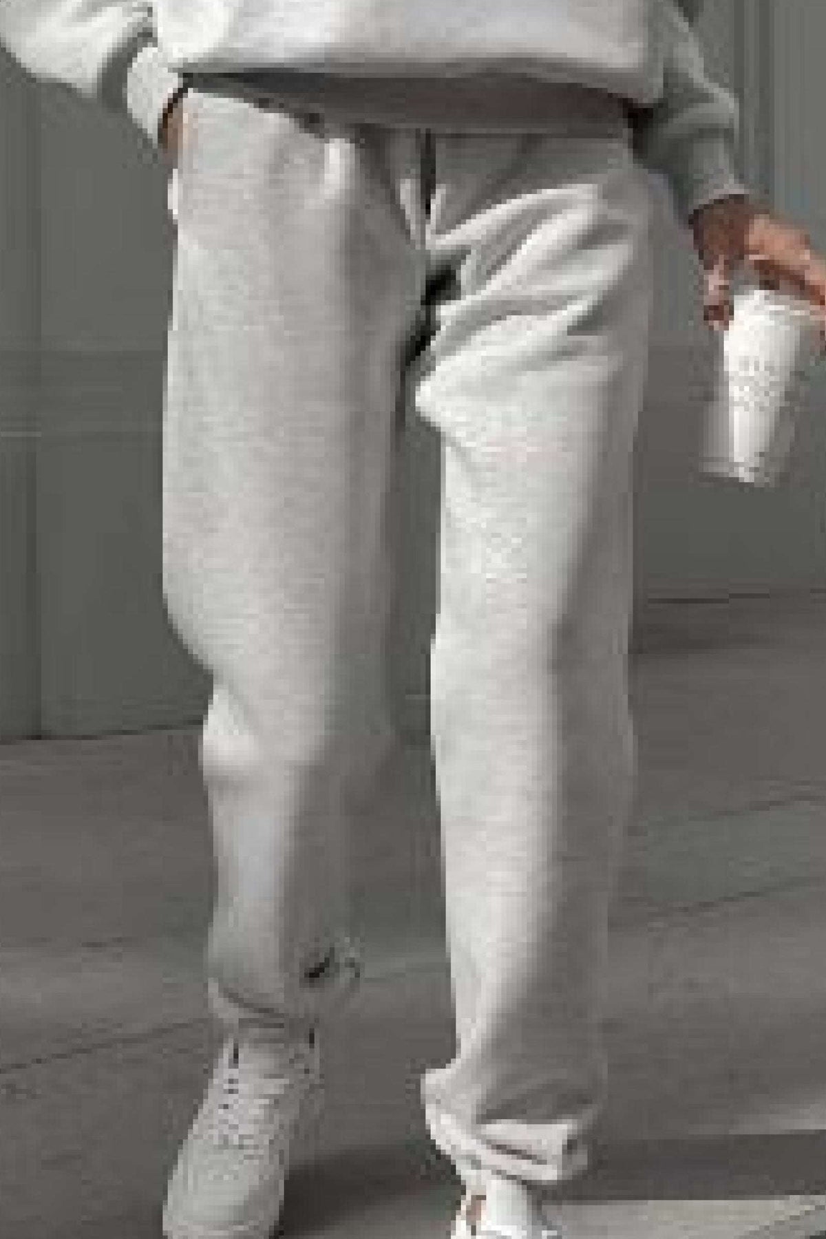Close-up of light gray cotton blend tracksuit pants worn with white sneakers, casual loungewear style.