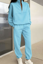 Woman wearing light blue cotton blend tracksuit with zip neckline and white sneakers standing indoors